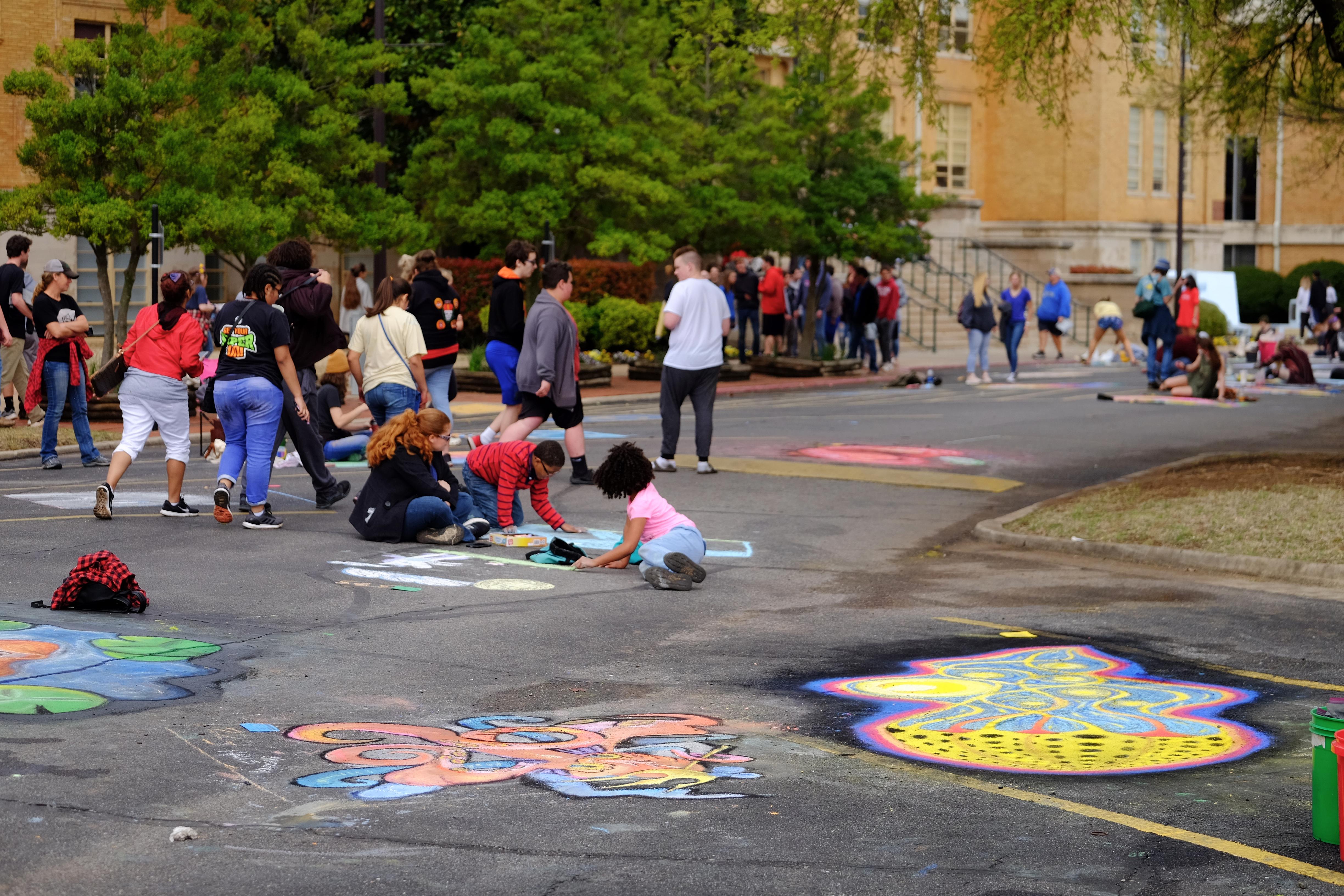 Crowd of people walking by and drawing with chalk