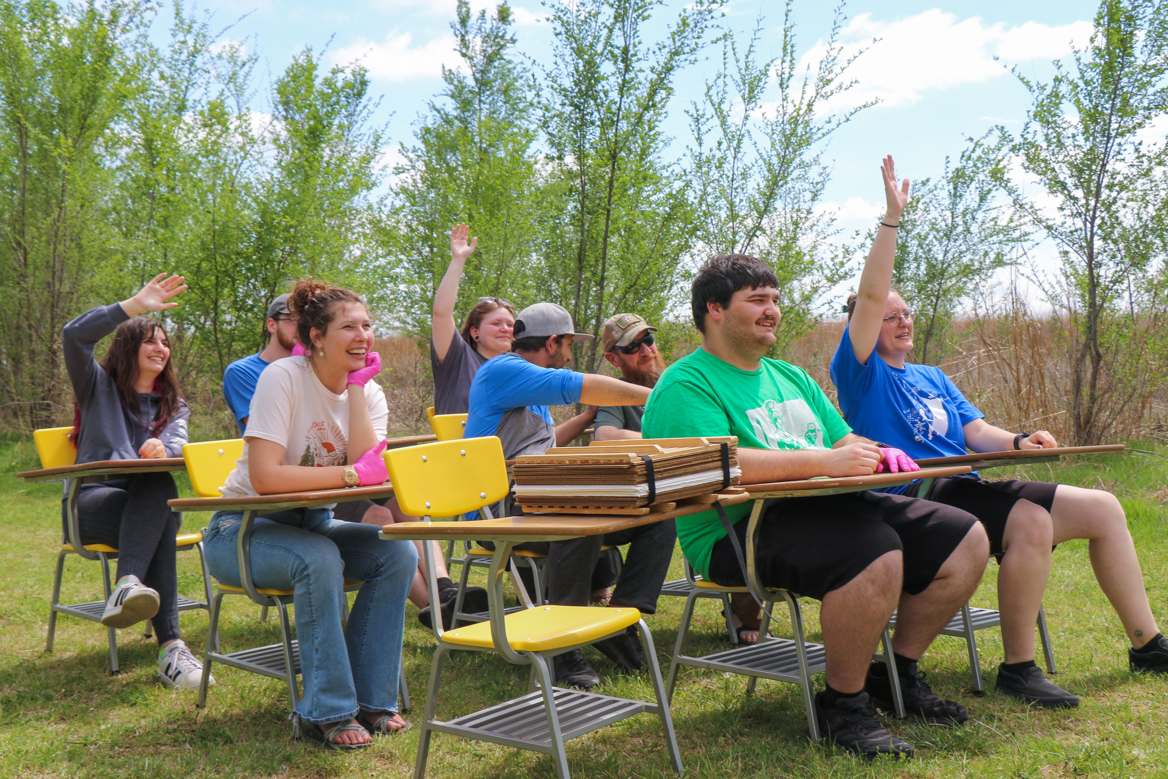 Students sitting outside and raising their hands. 