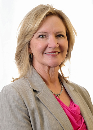 Kelly Wilkerson smiling and facing the camera. Photo is a headshot of Kelly with him in a pink blouse and light grey blazer.