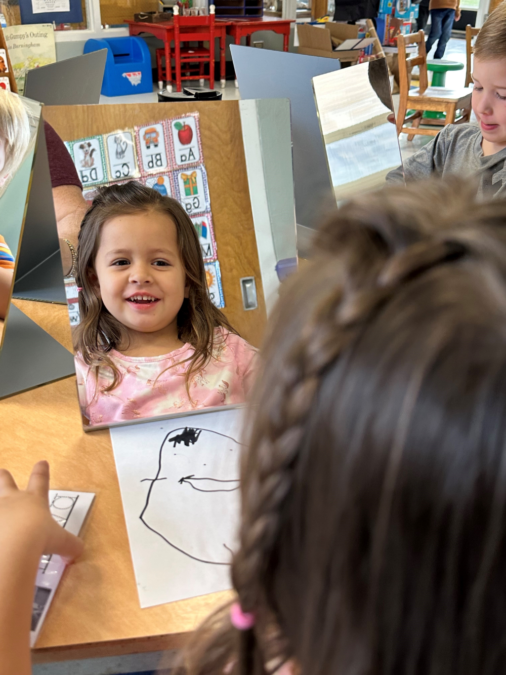 A child smiling at themself in a tabletop mirror.