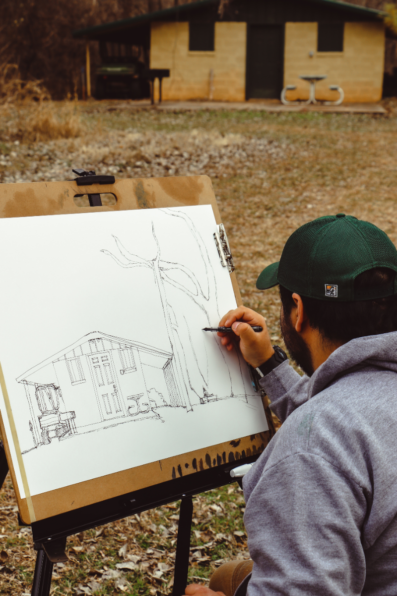 Student sitting outside with an easel drawing a building. 