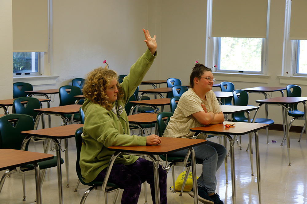 Two workshop participants sitting at desks, one with a hand raised to ask a question