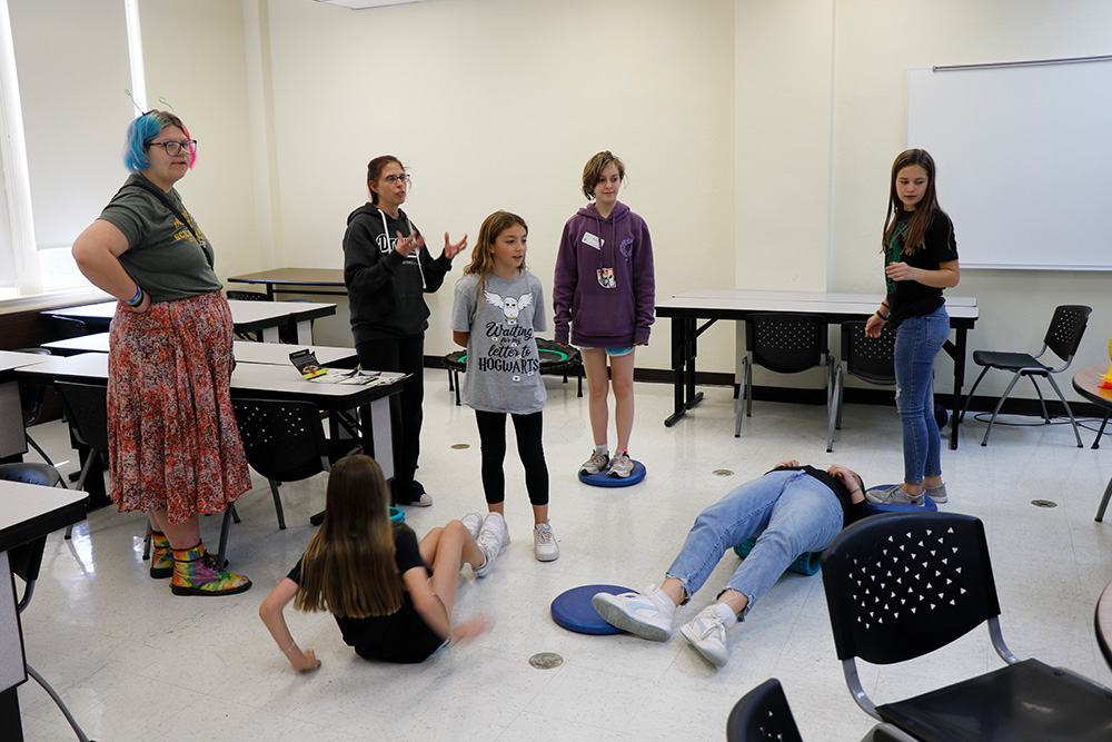 Seven workshop participants observe, and interact with equipment on the floor of a classroom