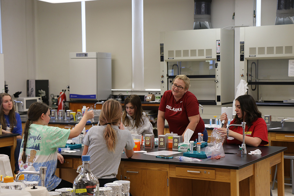 Instructor smiles while conversing with a student, while other students practice working with pipettes