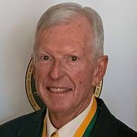 Eugene Earsom wearing a black blazer over a green and gold shirt, smiling to the camera.