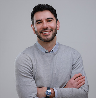 Smiling man with arms crossed in a light grey sweater