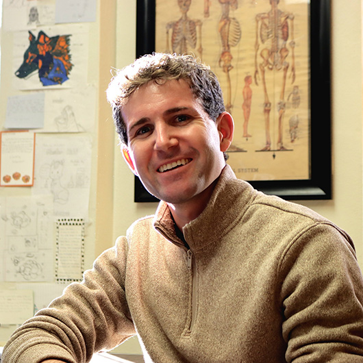 Man with curly brown hair wearing a tan quarter-zip sweater