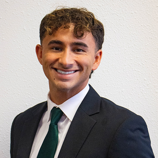 Man with curly hair wearing a suit and green tie smiling.