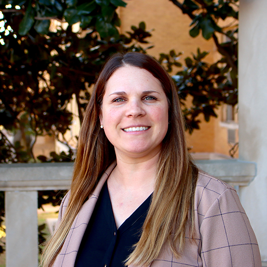 Smiling woman with medium brown hair, wearing a dark blue shirt and mauve jacket