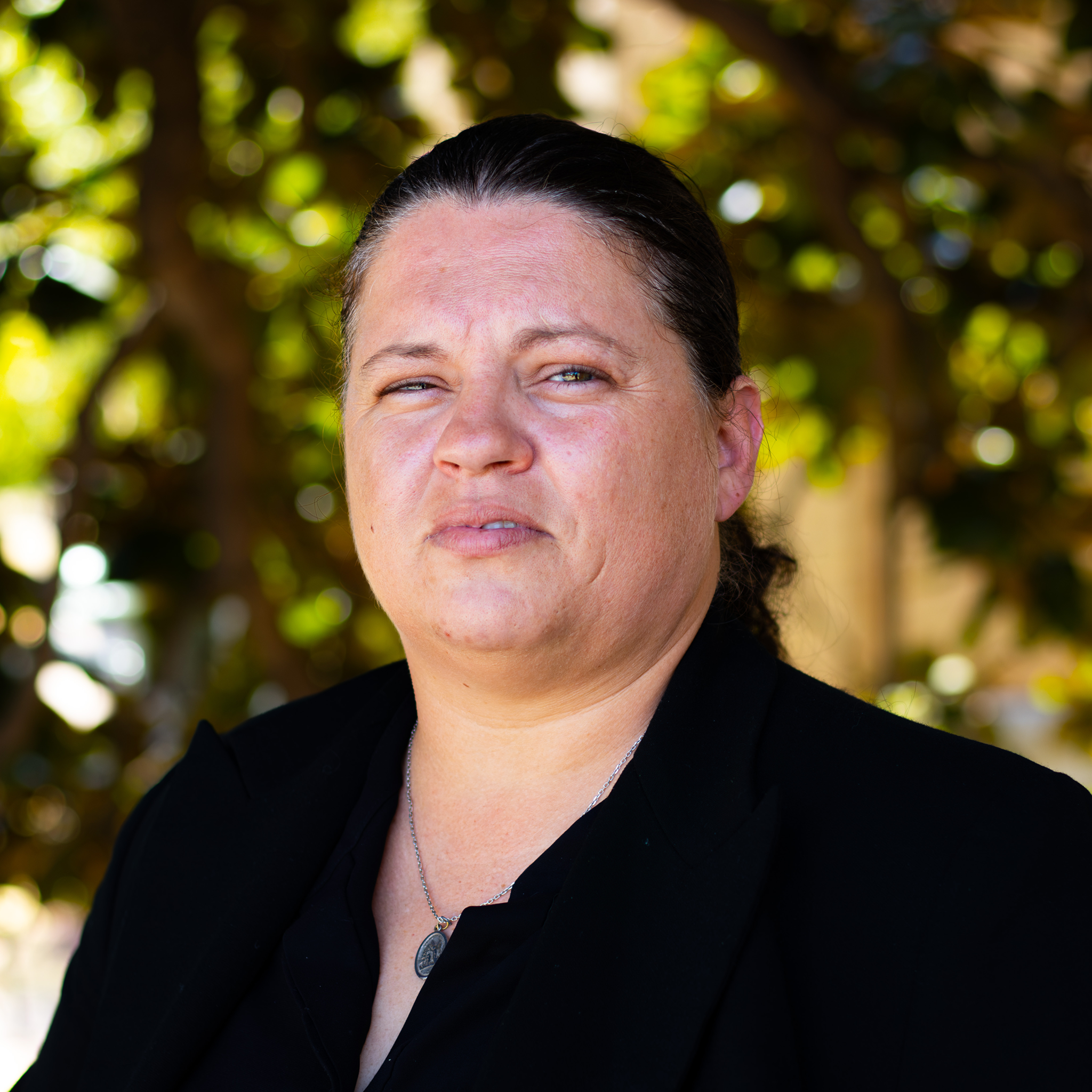 A woman standing in a black button-up shirt in front of the tree