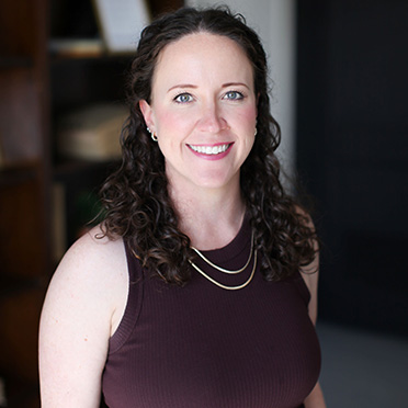 Smiling woman in a brown shirt and two gold necklaces