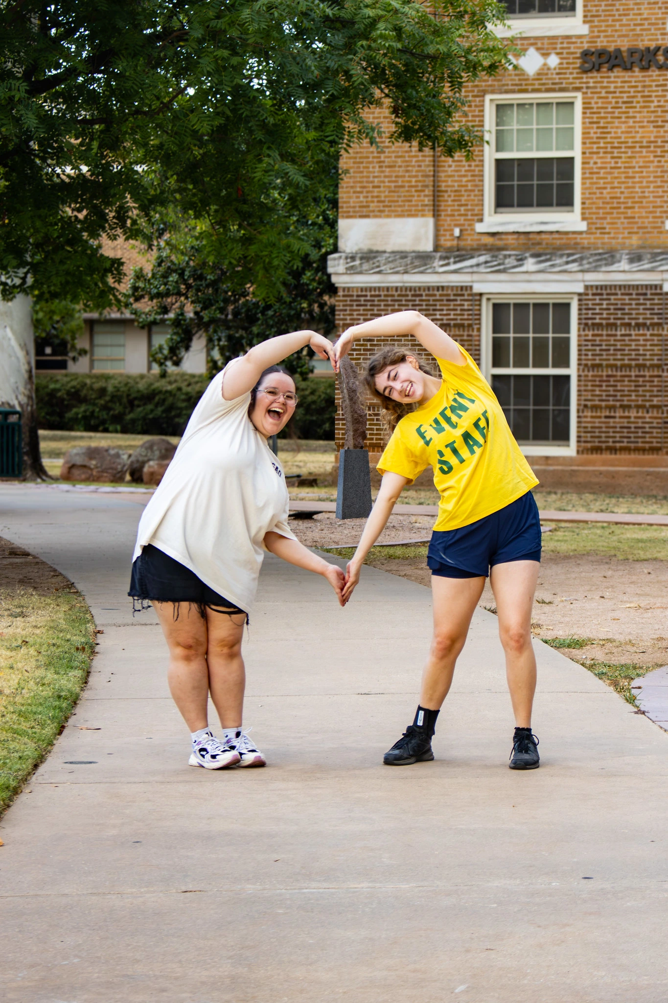 Two students form a heart with their arms outside Sparks Hall on the USAO campus.