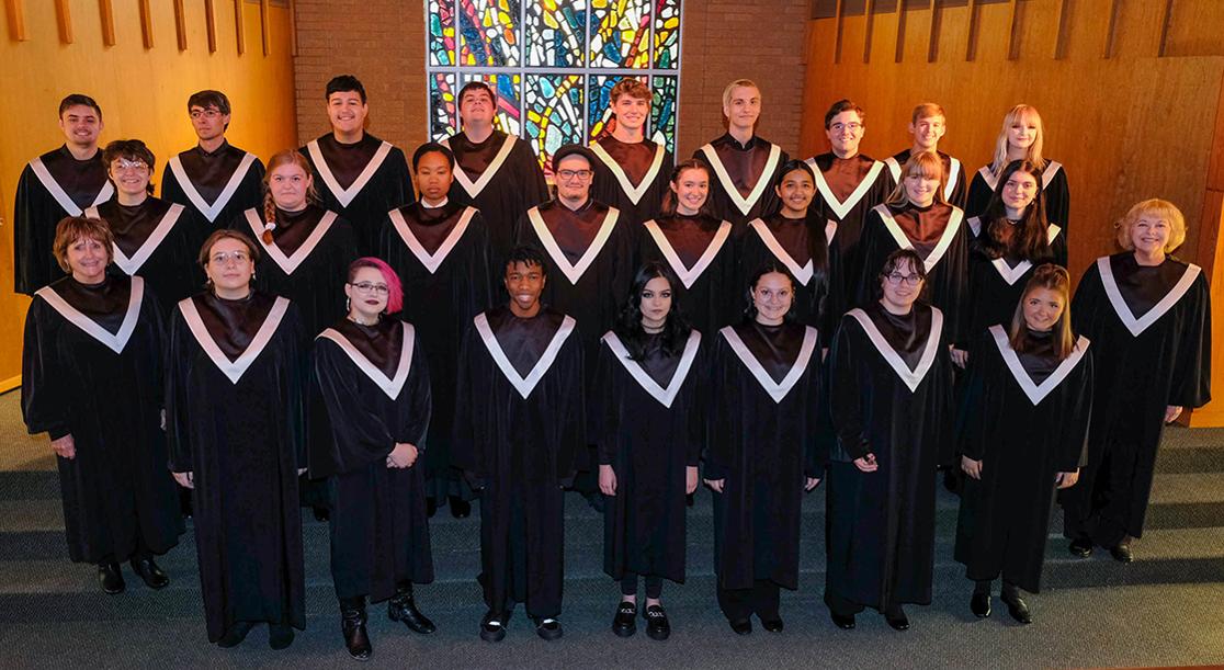 Three rows of students in black robes on the steps of the Alumni Chapel stage