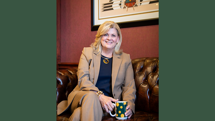 President Kayla Hale sitting on a couch with her legs crossed, holding a coffee cup. 