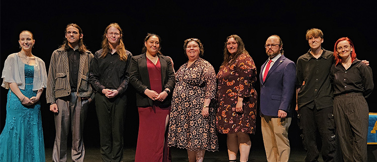 Eight people stand on stage in a line facing the audience
