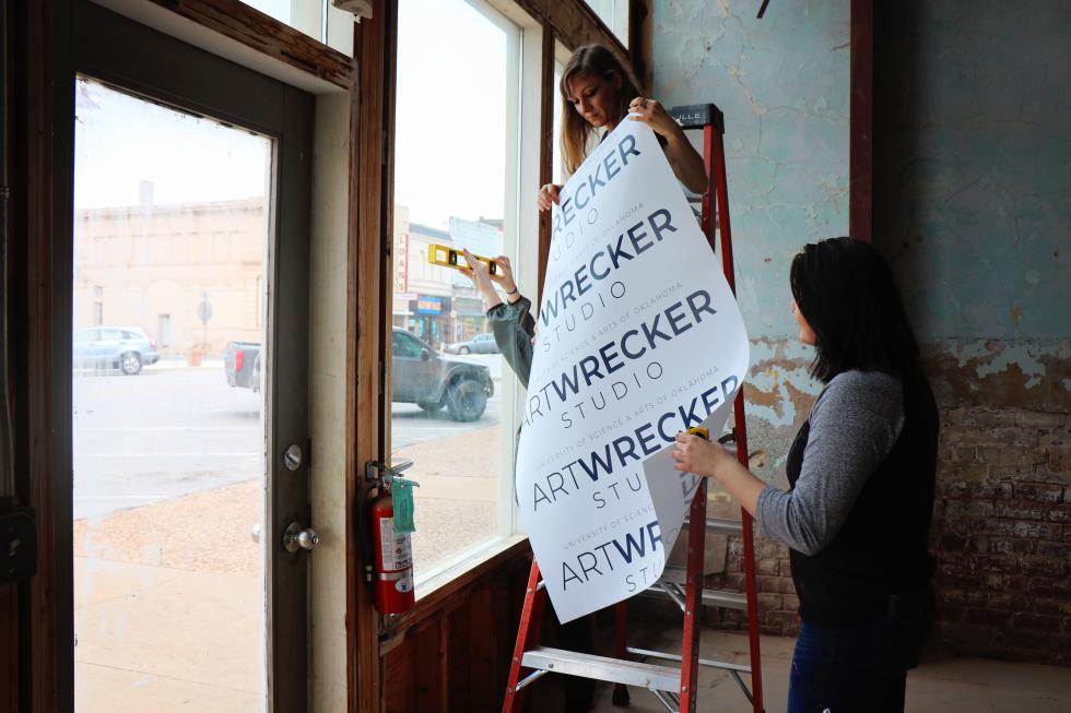 two women hanging banner with "Art Wrecker" on it 