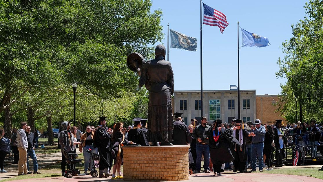 A photo of graduates, their families and faculty mingling near the Te Ata statue and Owens Flag Plaza after USAO's 2023 commencement ceremony