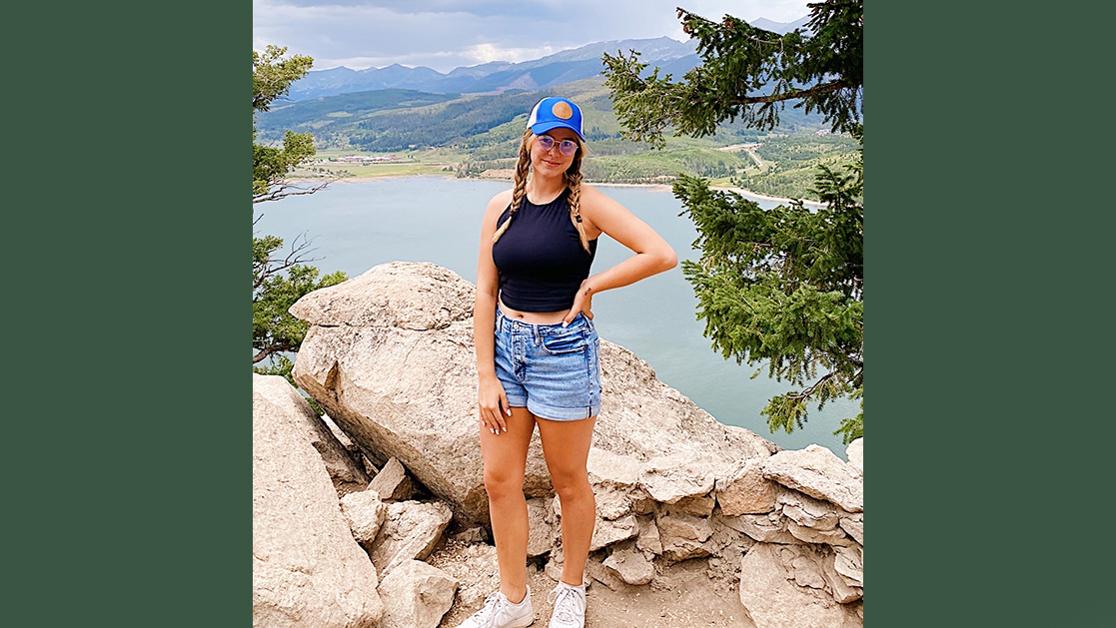 A photo of Hannah Dudleson standing in front of an outcropping that overlooks a large tropical lake