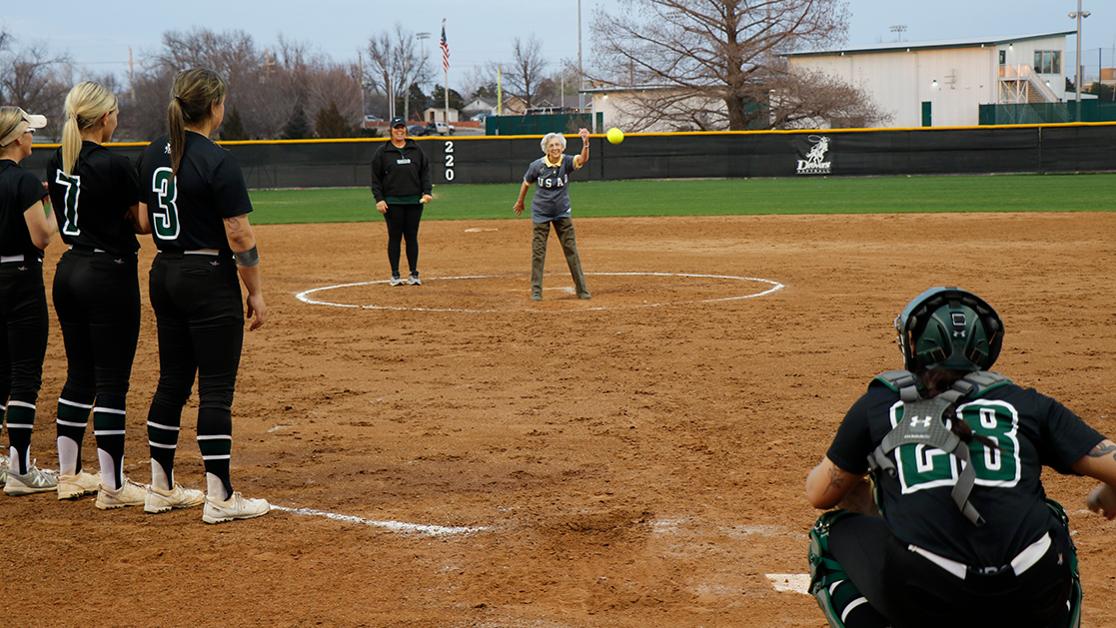 A photo of alumna Dr. Kathy Black throwing the first pitch at a special softball game with current Drover players cheering her on