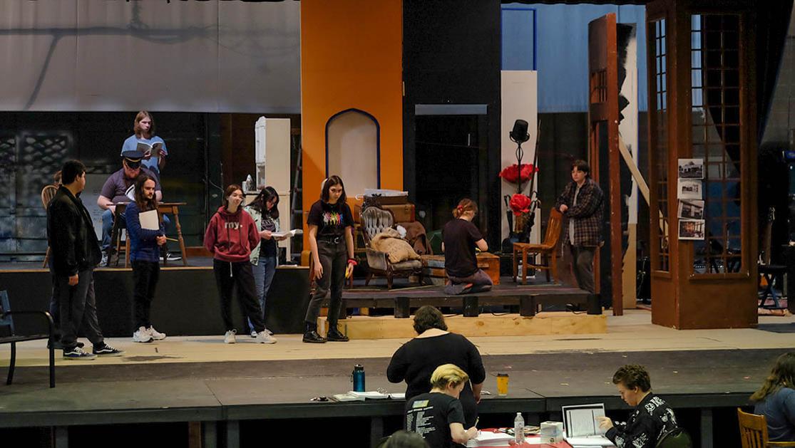 A photo of students in the spring theater production on a rough stage taking direction from Professor Katie Davis