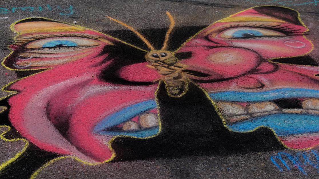 Chalk art showing a colorful butterfly with a crazed face making up its wing pattern