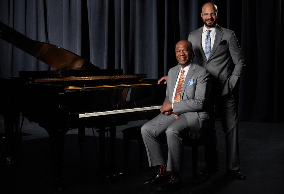 A photo of Donald Ryan seated by a grand piano with his son Barron standing beside him