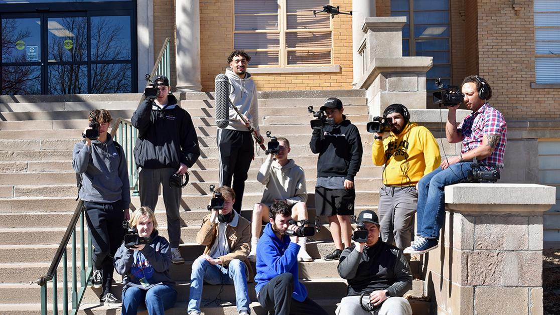 A photo of students in USAO's video production program on the Troutt Hall steps with various camera, mics and other video equipment in their hands